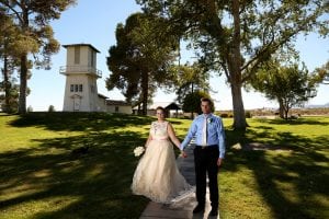 A bride and groom walking down a path in front of a clock tower.
