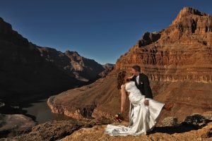 A bride and groom standing on a cliff overlooking the grand canyon.