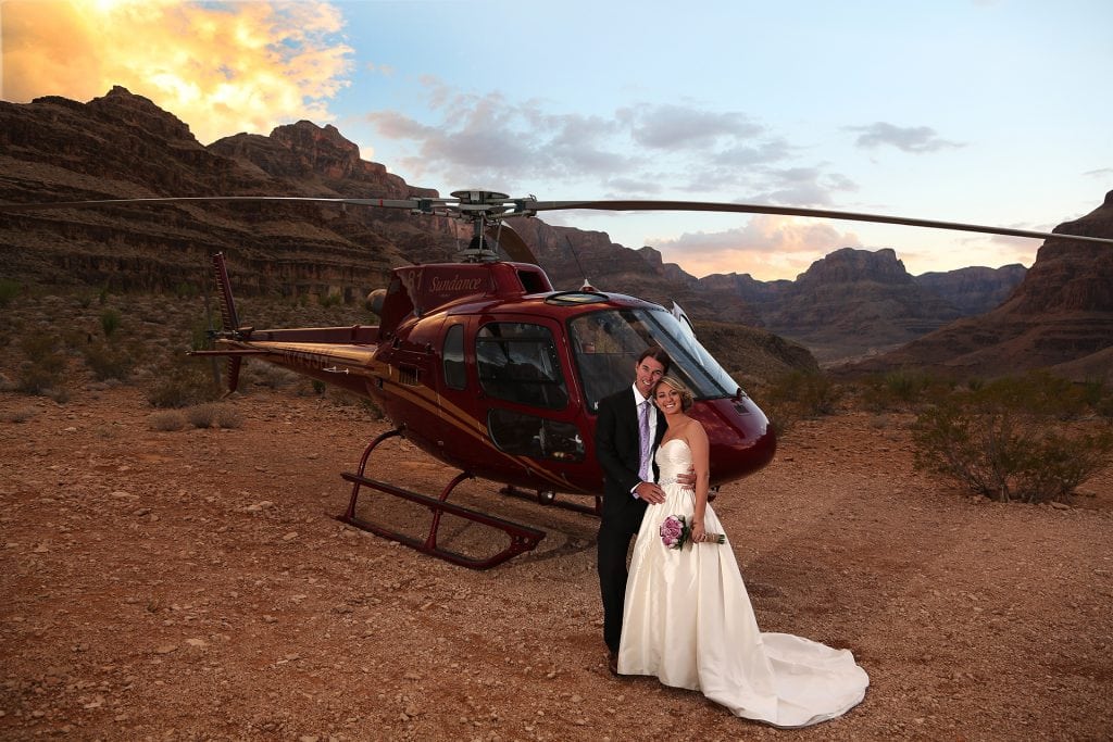 A bride and groom standing in front of a helicopter.