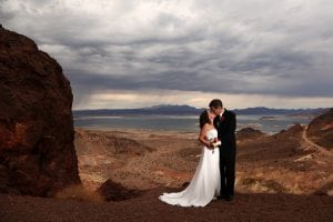 A bride and groom standing on a cliff overlooking a lake.