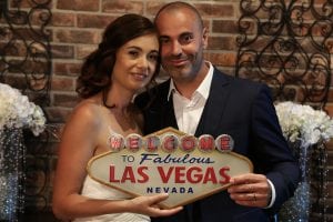 A bride and groom pose with a welcome to las vegas sign.
