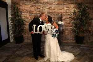 A bride and groom kissing in front of a love sign.