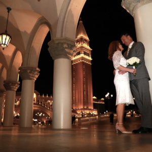 A bride and groom standing in front of an archway at night.