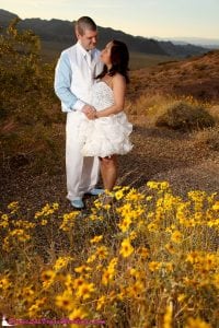 A bride and groom are posing in front of colorful flowers at Lake Mead.