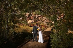A bride and groom standing on a wooden bridge.