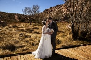 A bride and groom kissing on a wooden deck in the desert.