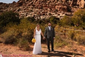 A bride and groom standing in front of a red rock formation.