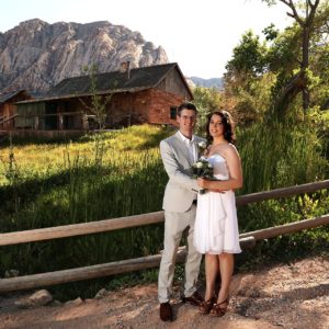 A bride and groom posing in front of a cabin.