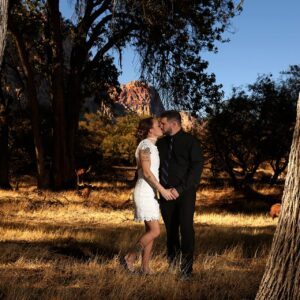A bride and groom kissing in the middle of a field of trees.