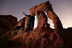 A bride and groom pose in front of a rock formation.