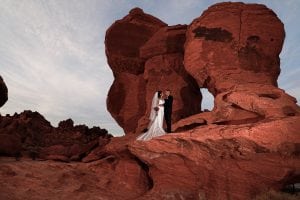 A bride and groom pose in front of a red rock formation.