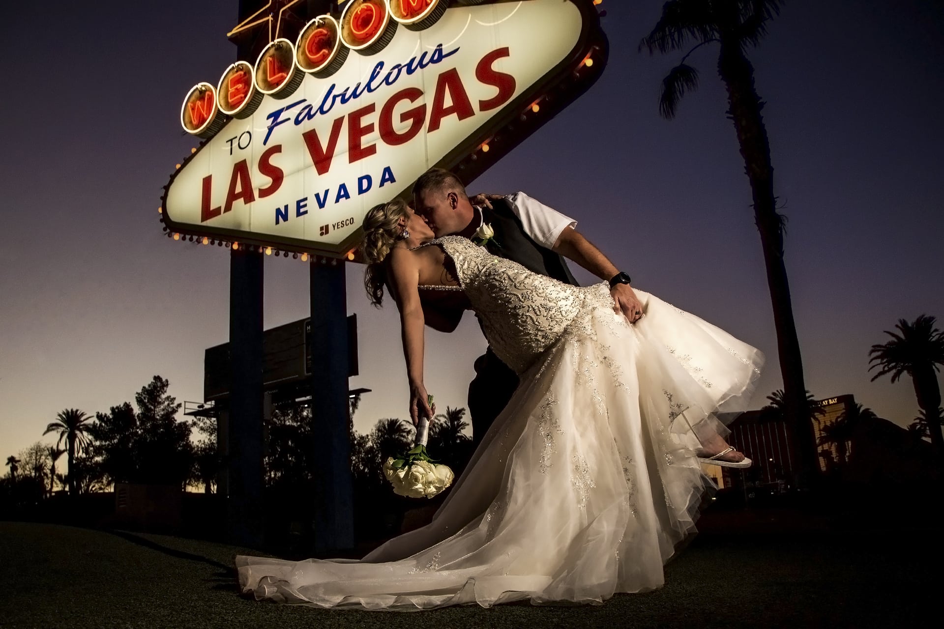 A bride and groom kiss in front of the las vegas sign.