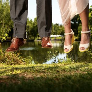 A bride and groom are jumping in the air in front of a pond.