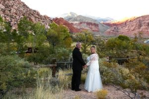 A bride and groom standing in front of a fence in red rock canyon.