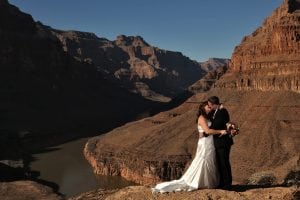 A bride and groom standing on a cliff overlooking the grand canyon.