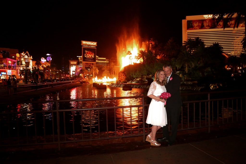 A bride and groom posing in front of a fire.