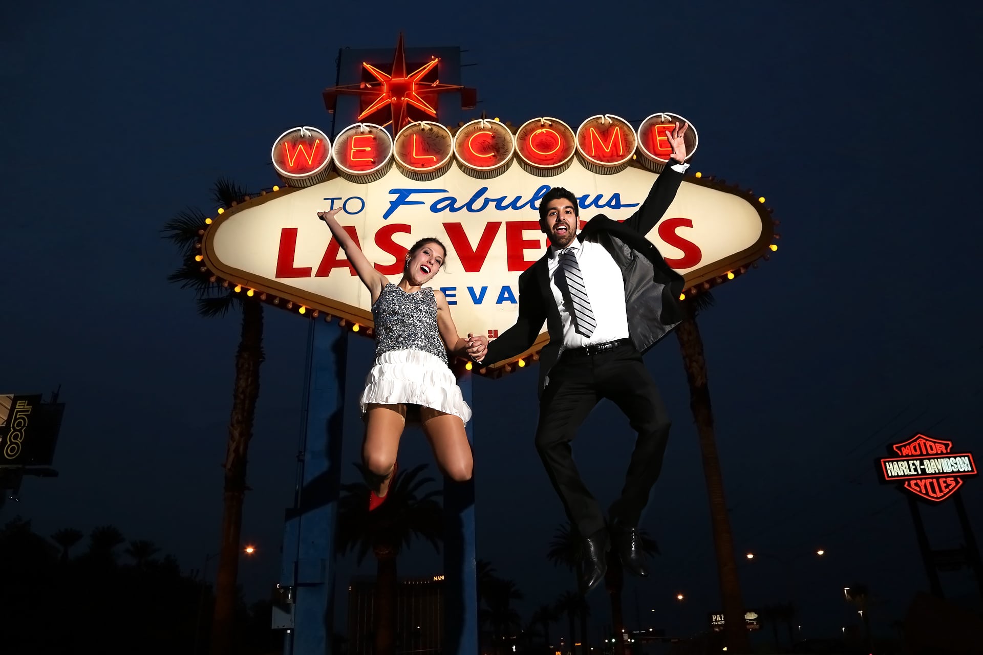 A couple jumping in front of the welcome to las vegas sign.