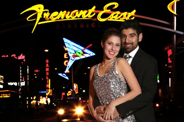 A couple posing in front of a neon sign.