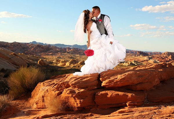A bride and groom kissing on a rock in the desert.