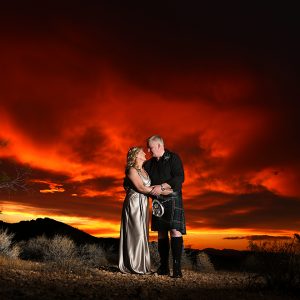 A bride and groom standing in front of a red sky at sunset.