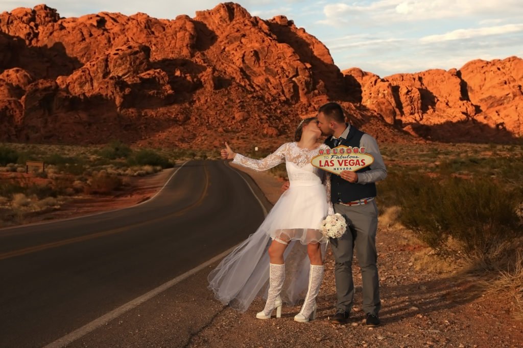 A bride and groom kissing on the road in front of a sign.