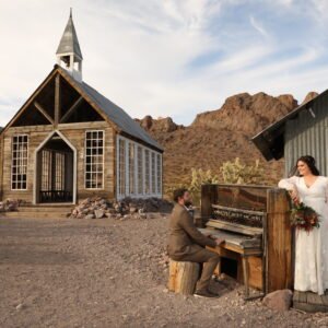 A bride and groom standing next to a piano in the desert.