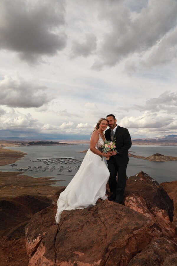 A bride and groom posing on top of a cliff overlooking lake las vegas.
