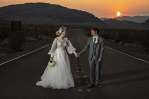 A bride and groom standing on a desert road at sunset during their Valley of Fire elopement.