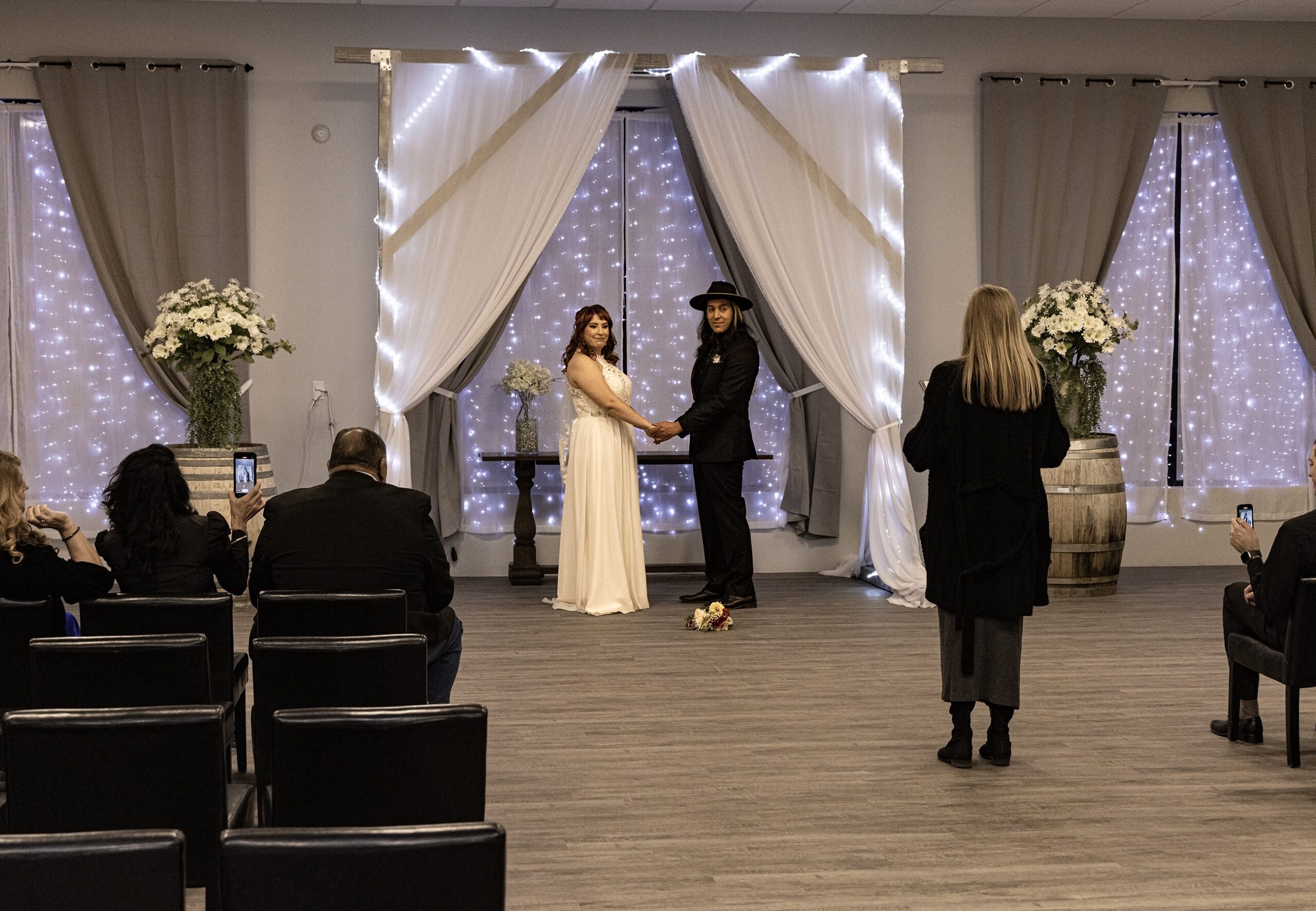 A couple holds hands at the altar in one of the Las Vegas wedding chapels during a ceremony while a woman officiates and guests look on.